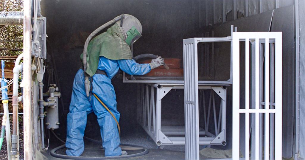Colortec technician in protective gear sand blasting metal parts